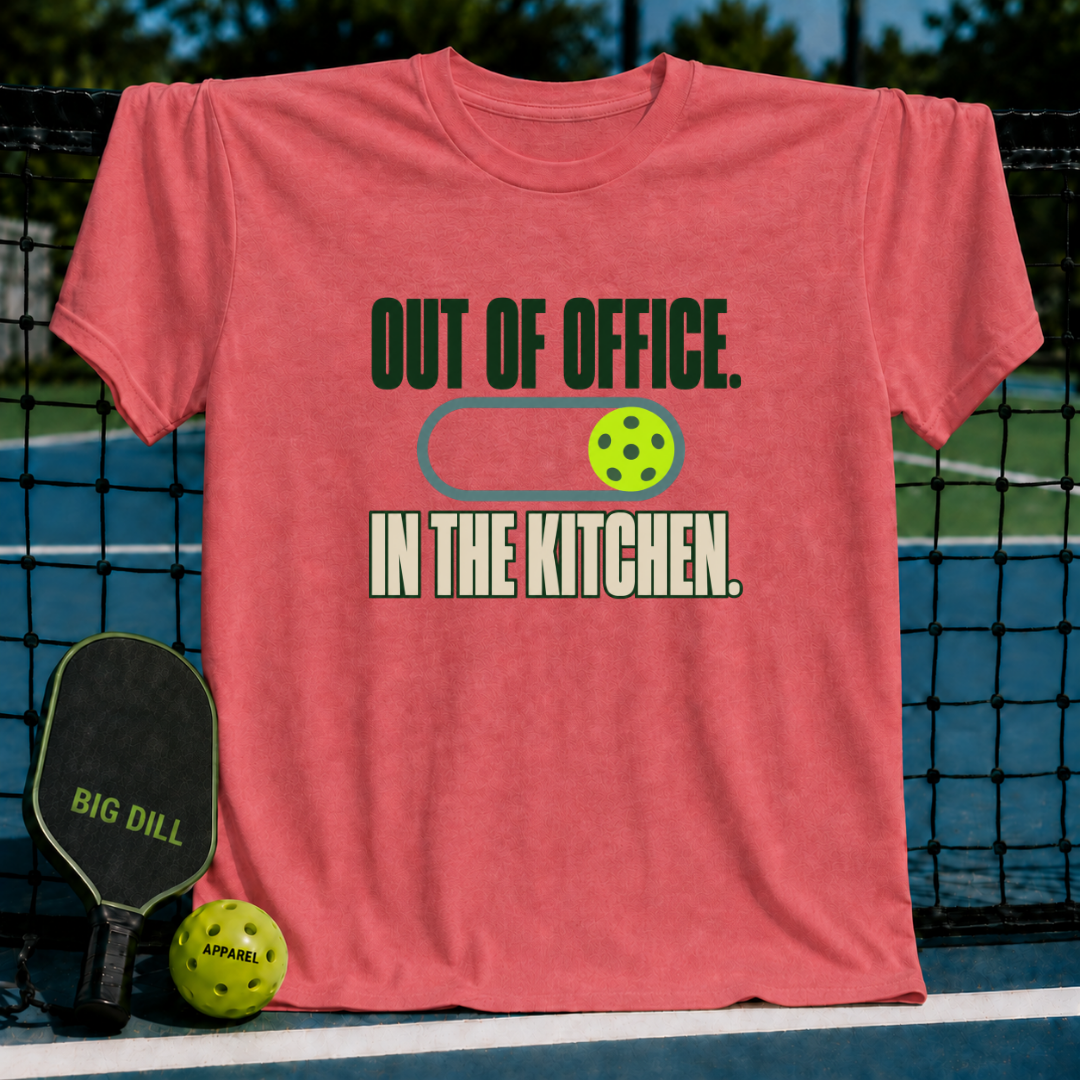 Coral crewneck t-shirt featuring Out of Office In the Kitchen text and a pickleball graphic on a court background.