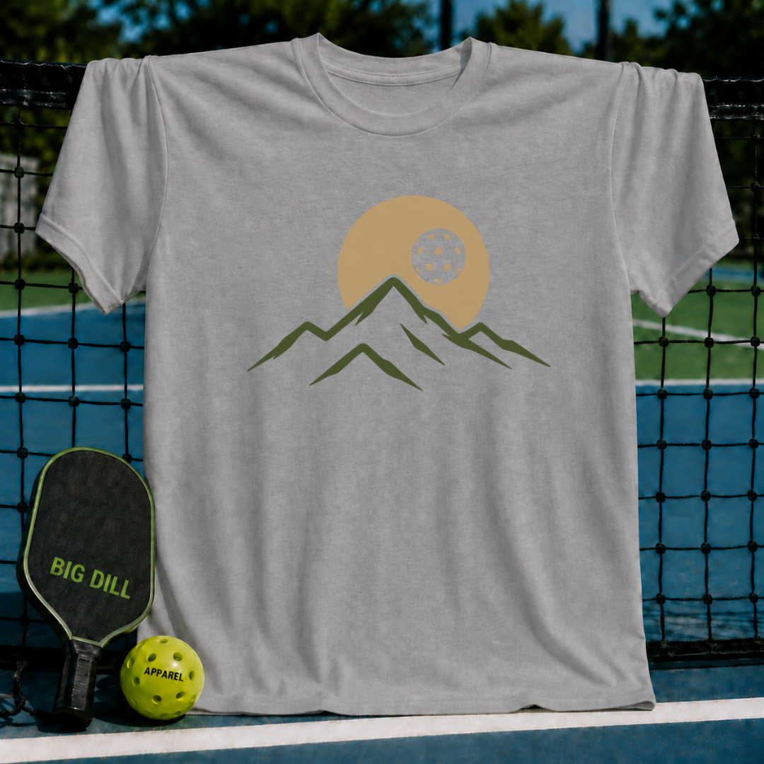 Light gray unisex t-shirt featuring a minimalist mountain and pickleball eclipse graphic, displayed on a pickleball court.