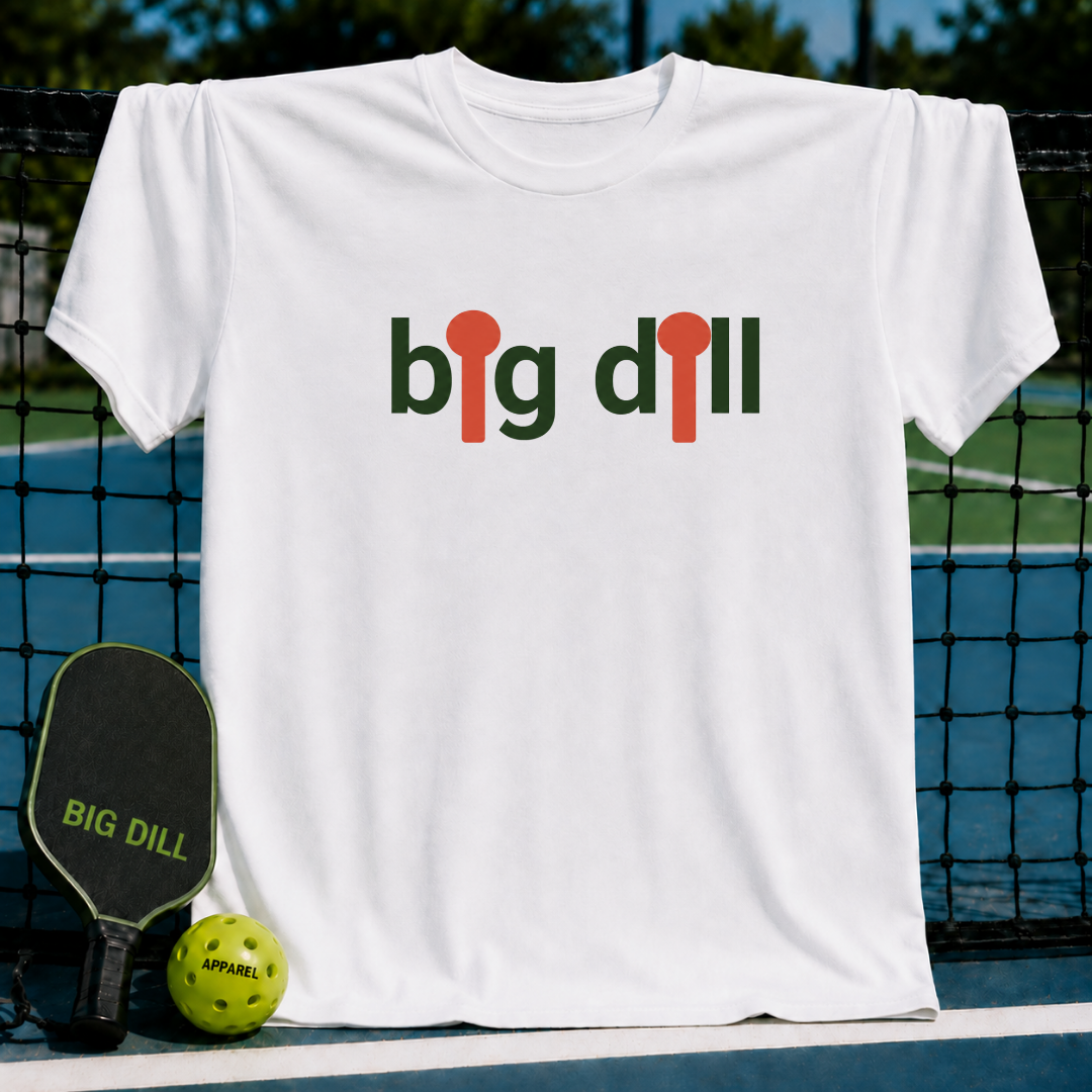 White unisex t-shirt featuring a Big Dill graphic with orange pickleball paddle icons on a pickleball court background.