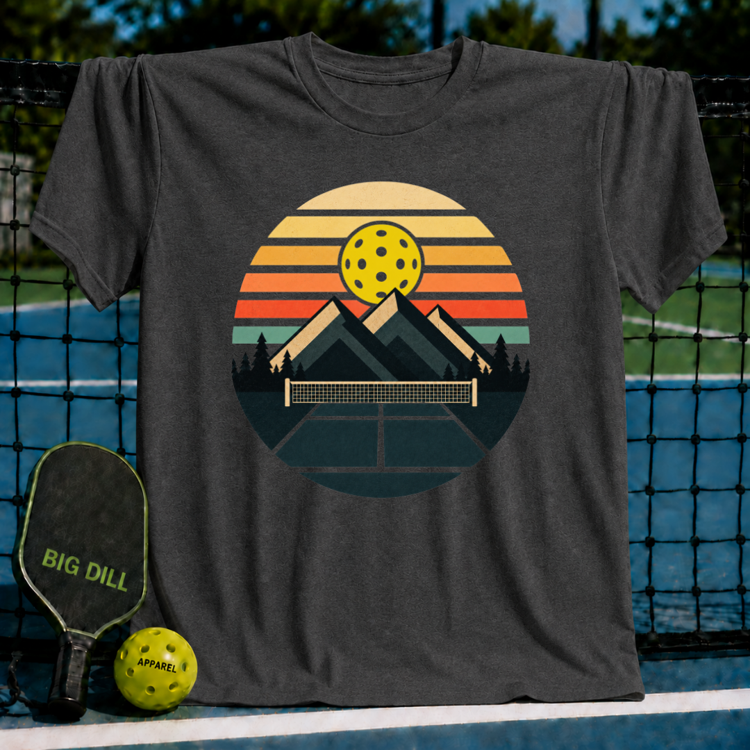 Black unisex t-shirt featuring a retro circular graphic of mountains, a pickleball net, and a sunset in orange and teal.