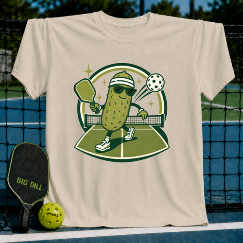 Beige crewneck t-shirt featuring a cartoon pickle wearing sunglasses and a headband playing pickleball on a court.