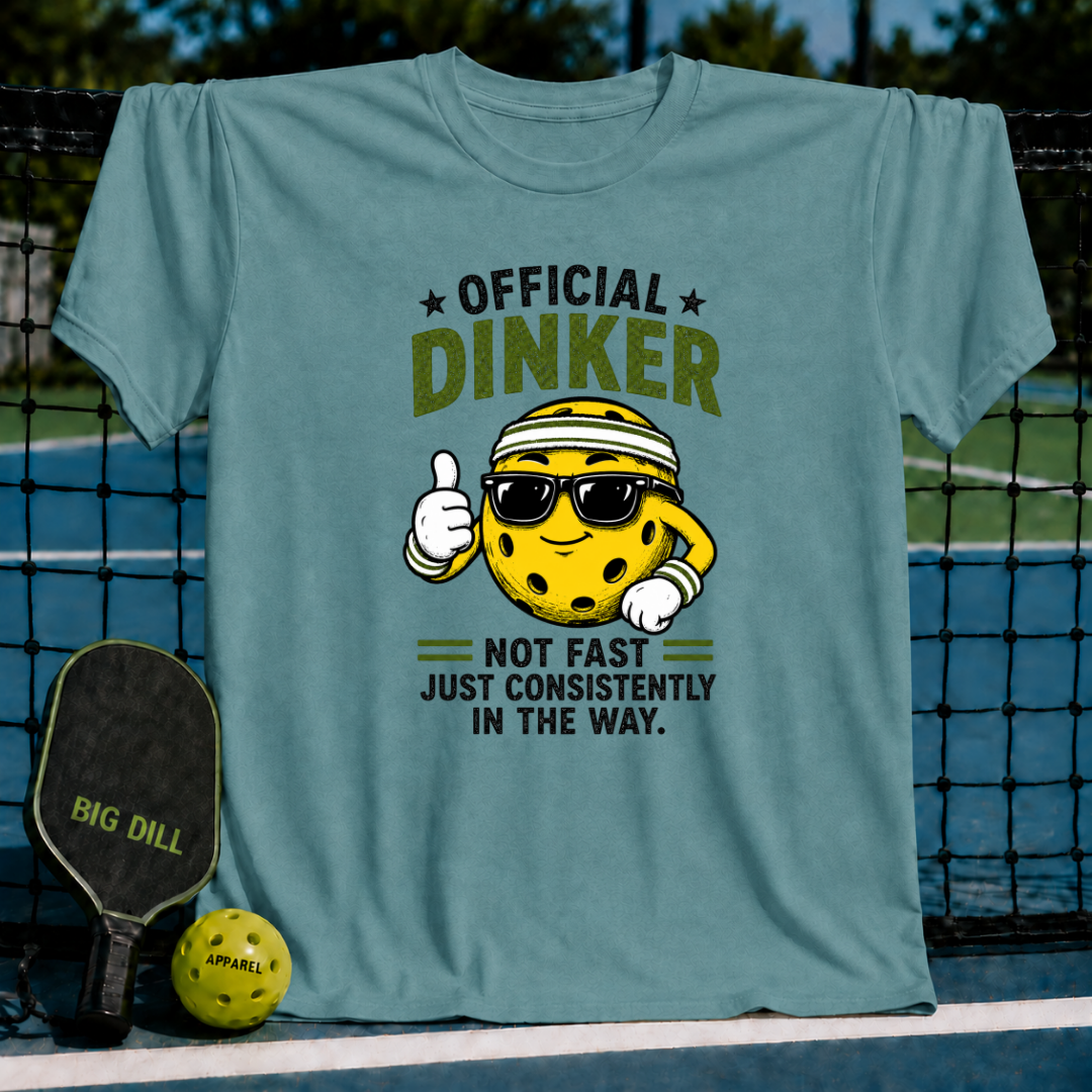 Dusty blue crewneck T-shirt featuring a cartoon pickleball character wearing sunglasses and a sweatband with Official Dinker text.