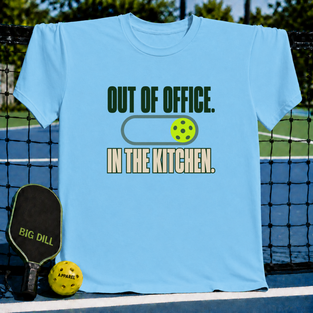 Light blue crew neck t-shirt featuring an Out of Office In the Kitchen pickleball graphic on a court background.