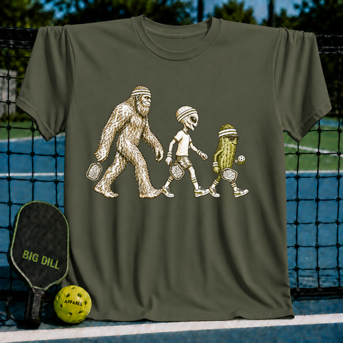 Olive green crewneck t-shirt featuring a graphic of Bigfoot, an alien, and a pickle playing pickleball on a court.