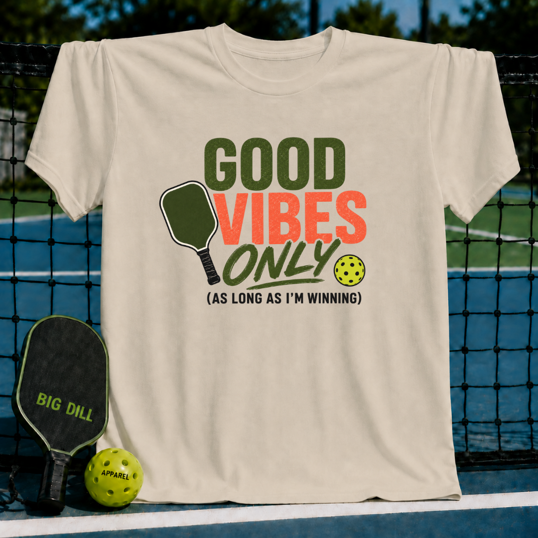 Cream unisex t-shirt featuring olive and rust text with a pickleball paddle and ball graphic on a court background.