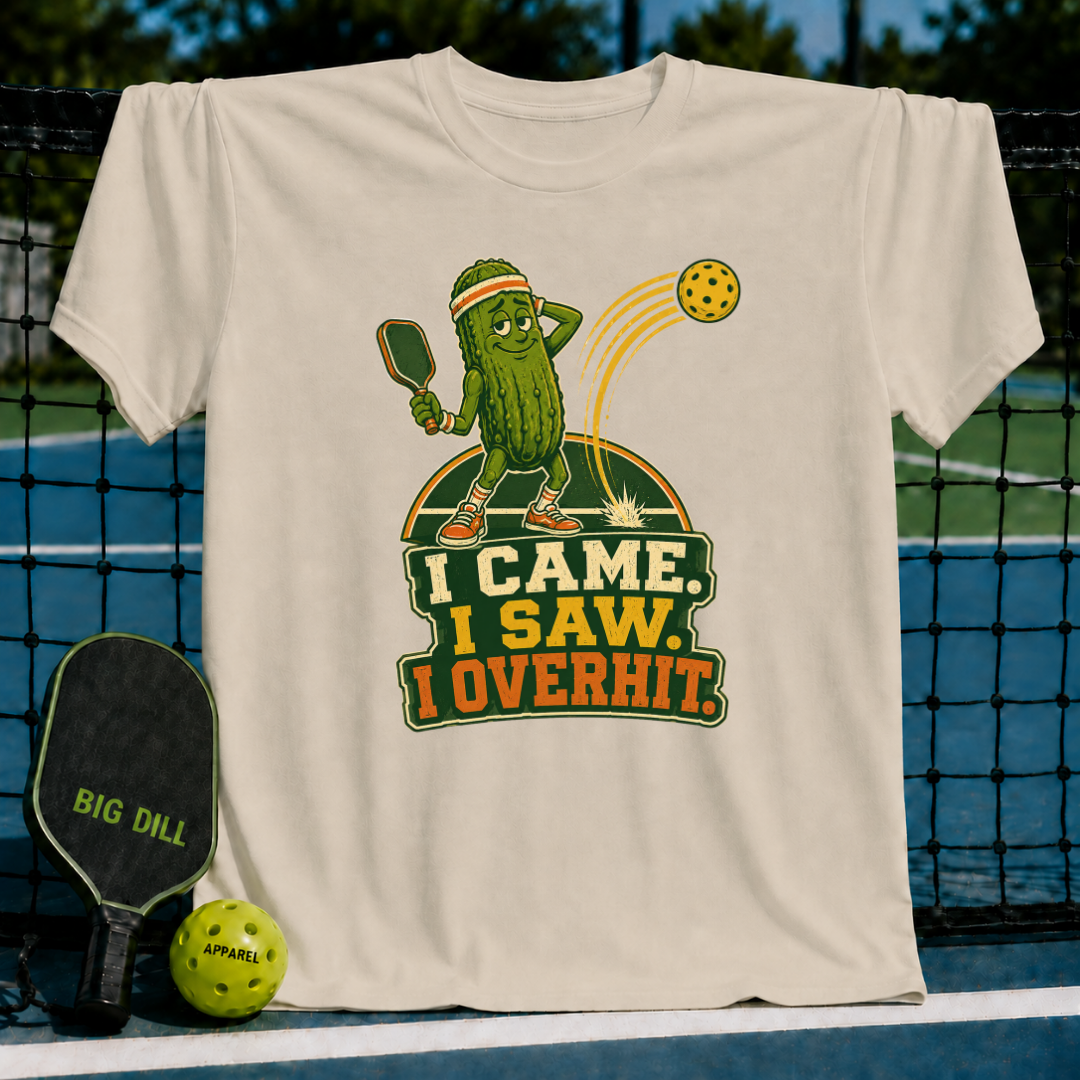 Beige Overhitter pickleball t-shirt featuring a cartoon pickle character playing pickleball with the text I Came, I Saw, I Overhit.