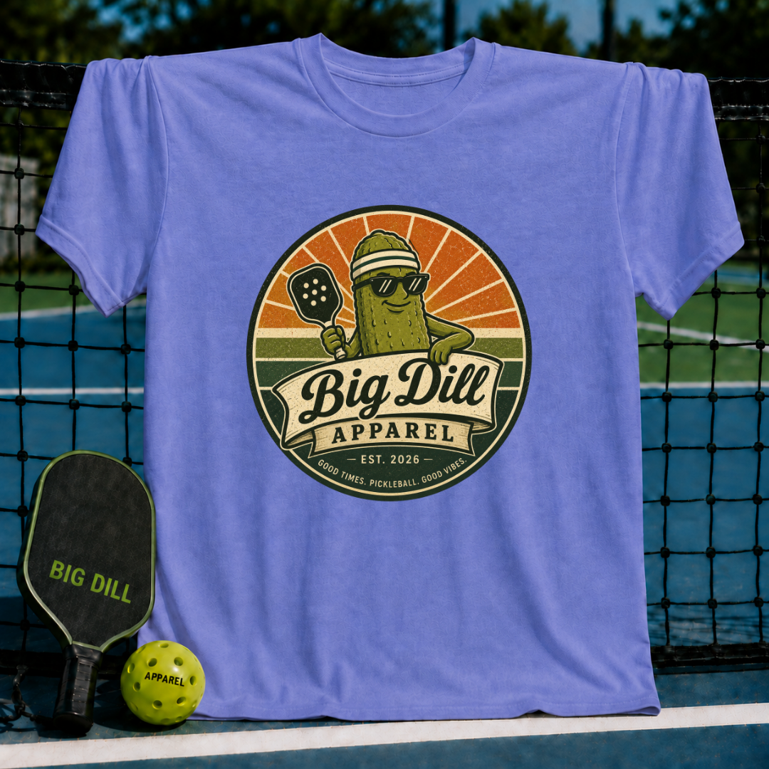 Periwinkle blue unisex t-shirt featuring a retro pickleball mascot graphic with a sunset badge design on a pickleball court.