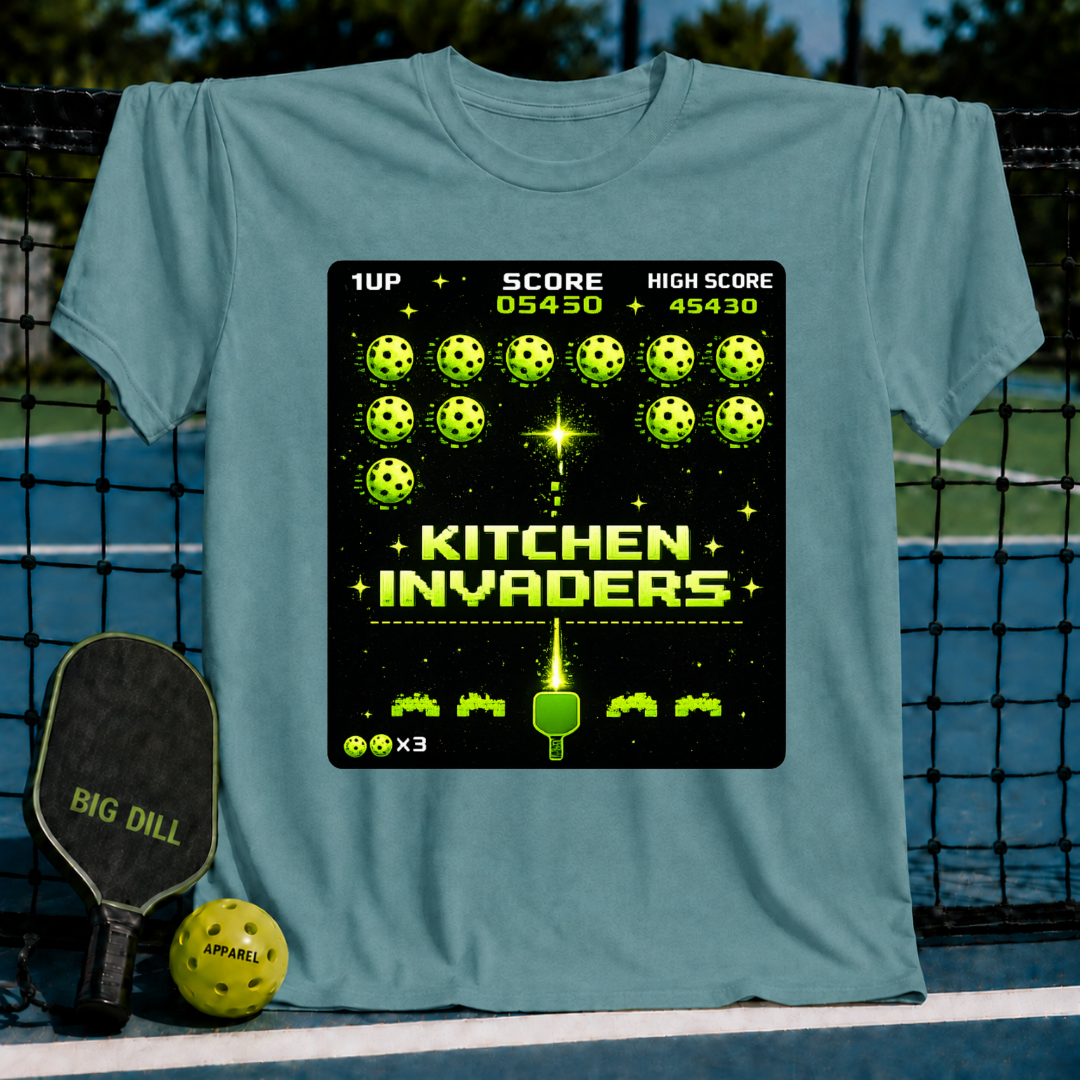 Blue-grey unisex t-shirt featuring a pixel-art Kitchen Invaders graphic with pickleballs and a paddle on a pickleball court.