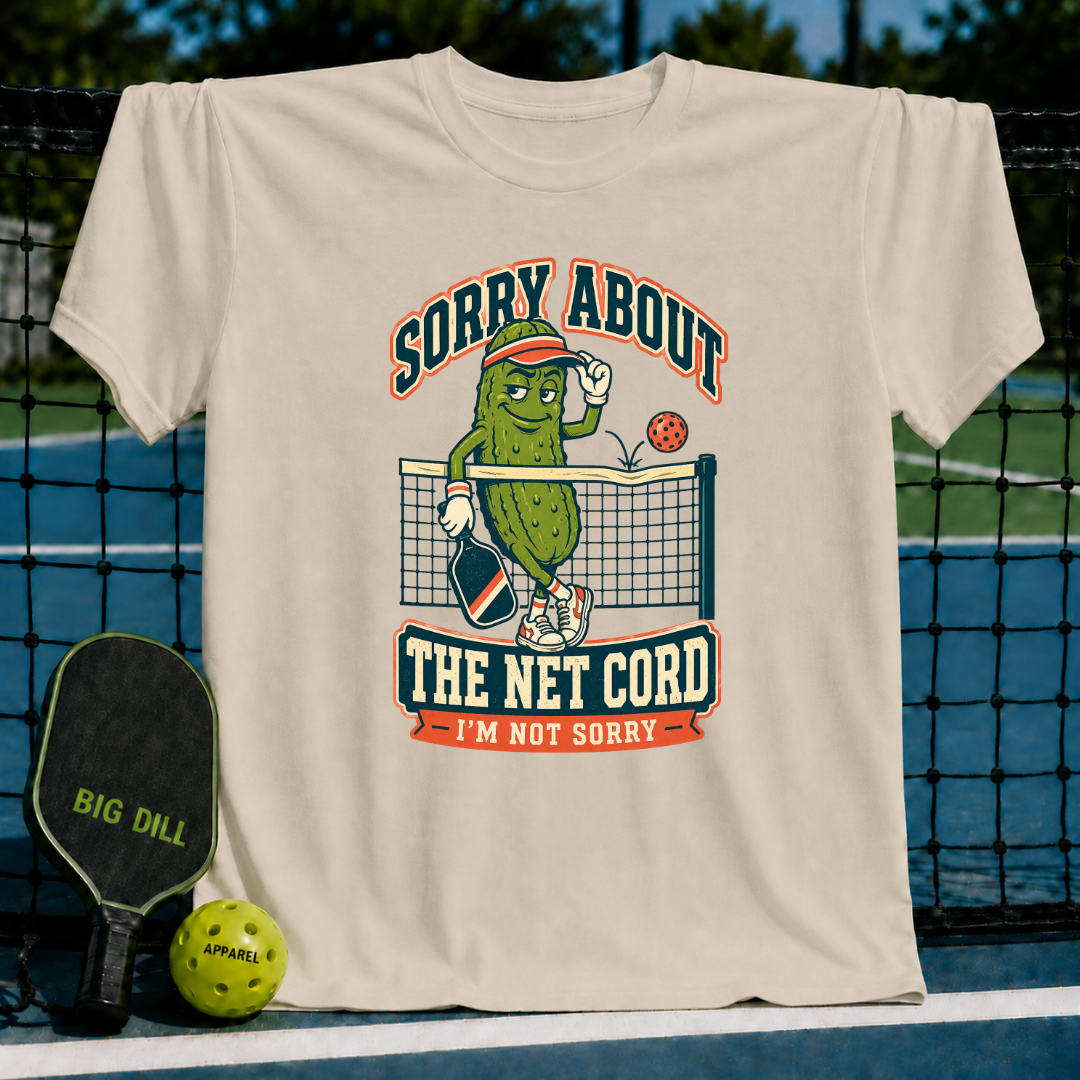 Beige crewneck t-shirt featuring a cartoon pickle playing pickleball with the text Sorry About The Net Cord.