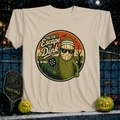 Sand-colored unisex t-shirt featuring a pickleball-themed Jason Voorhees pickle graphic with sunglasses and a paddle.