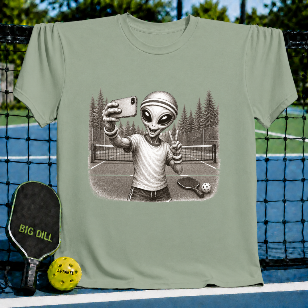 Sage green unisex t-shirt featuring a vintage-style illustration of an alien taking a selfie on a pickleball court.