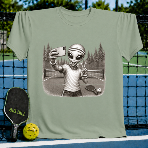 Sage green unisex t-shirt featuring a vintage-style illustration of an alien taking a selfie on a pickleball court.