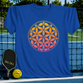 Blue t-shirt featuring an orange and yellow Flower of Life design made of pickleball paddles and balls on a court background.