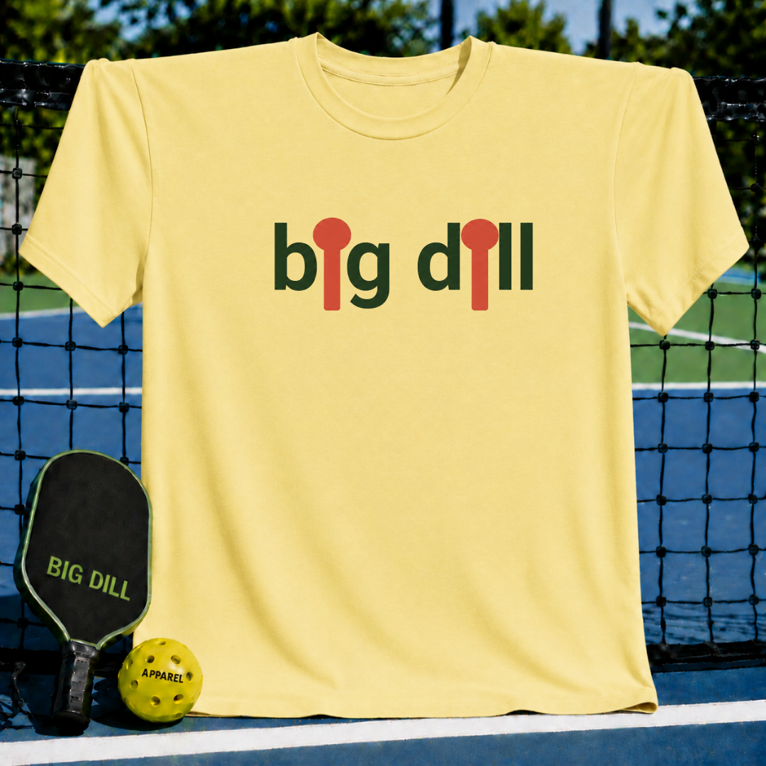 Soft yellow unisex t-shirt featuring a Big Dill graphic with red pickleball paddle icons, displayed on a pickleball court.