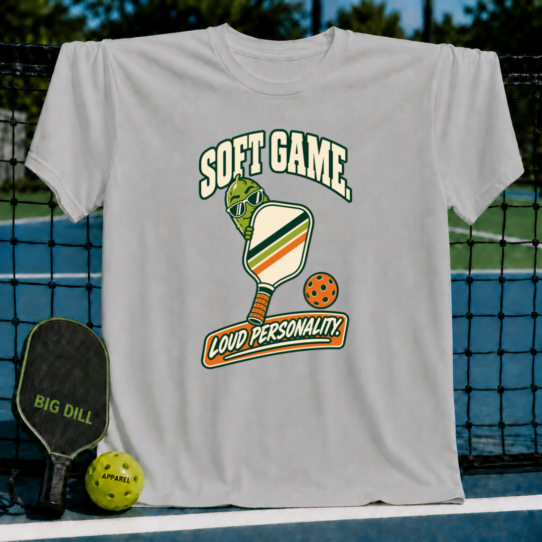 Light gray cotton t-shirt featuring a pickleball-themed graphic with a pickle character, paddle, and Soft Game text.