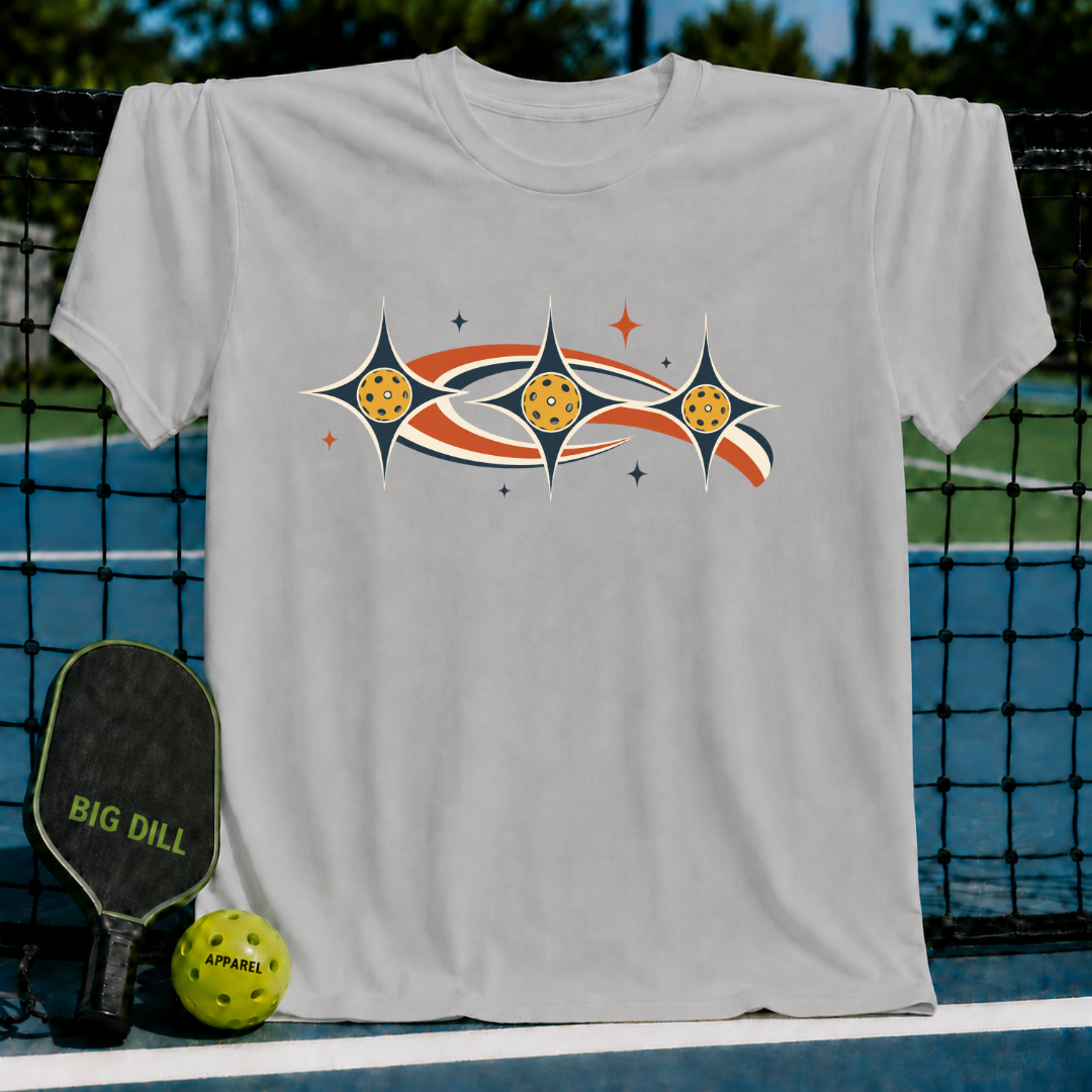 Light gray unisex t-shirt featuring a retro celestial pickleball graphic with stars and earth-toned swooshes on a court.