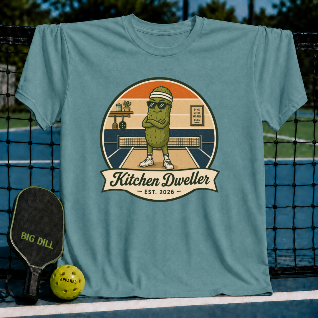 Periwinkle blue unisex t-shirt featuring a retro pickleball graphic of a pickle character in sunglasses at the kitchen line.