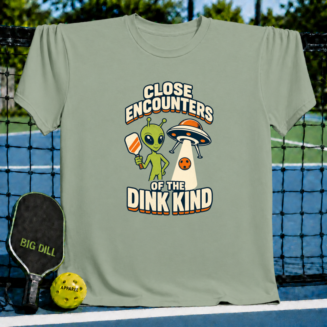Sage green cotton t-shirt featuring a cartoon alien holding a pickleball paddle and a UFO graphic with retro text.