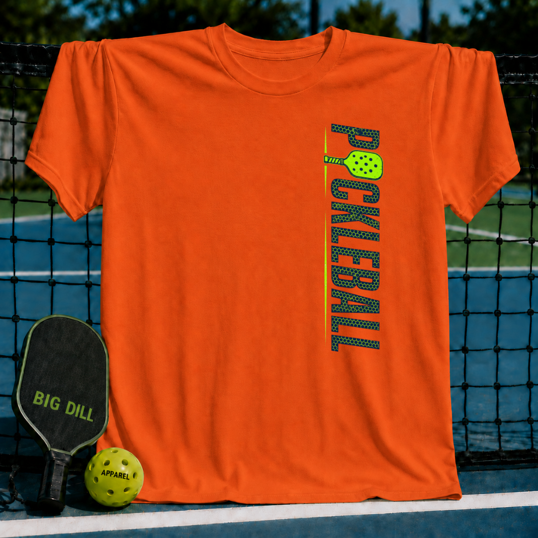 Bright orange unisex pickleball t-shirt with a vertical green graphic, displayed on a court with a paddle and ball.