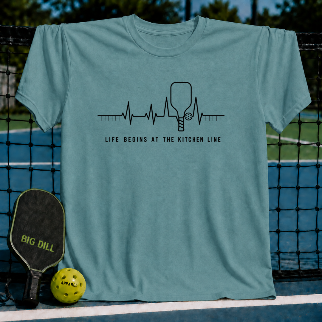 Blue-grey unisex t-shirt featuring a black heartbeat graphic with a pickleball paddle and text on a court background.