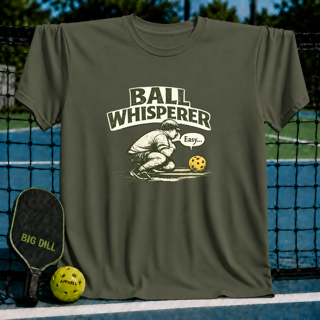 Olive green unisex t-shirt featuring a vintage Ball Whisperer illustration with collegiate lettering on a pickleball court.