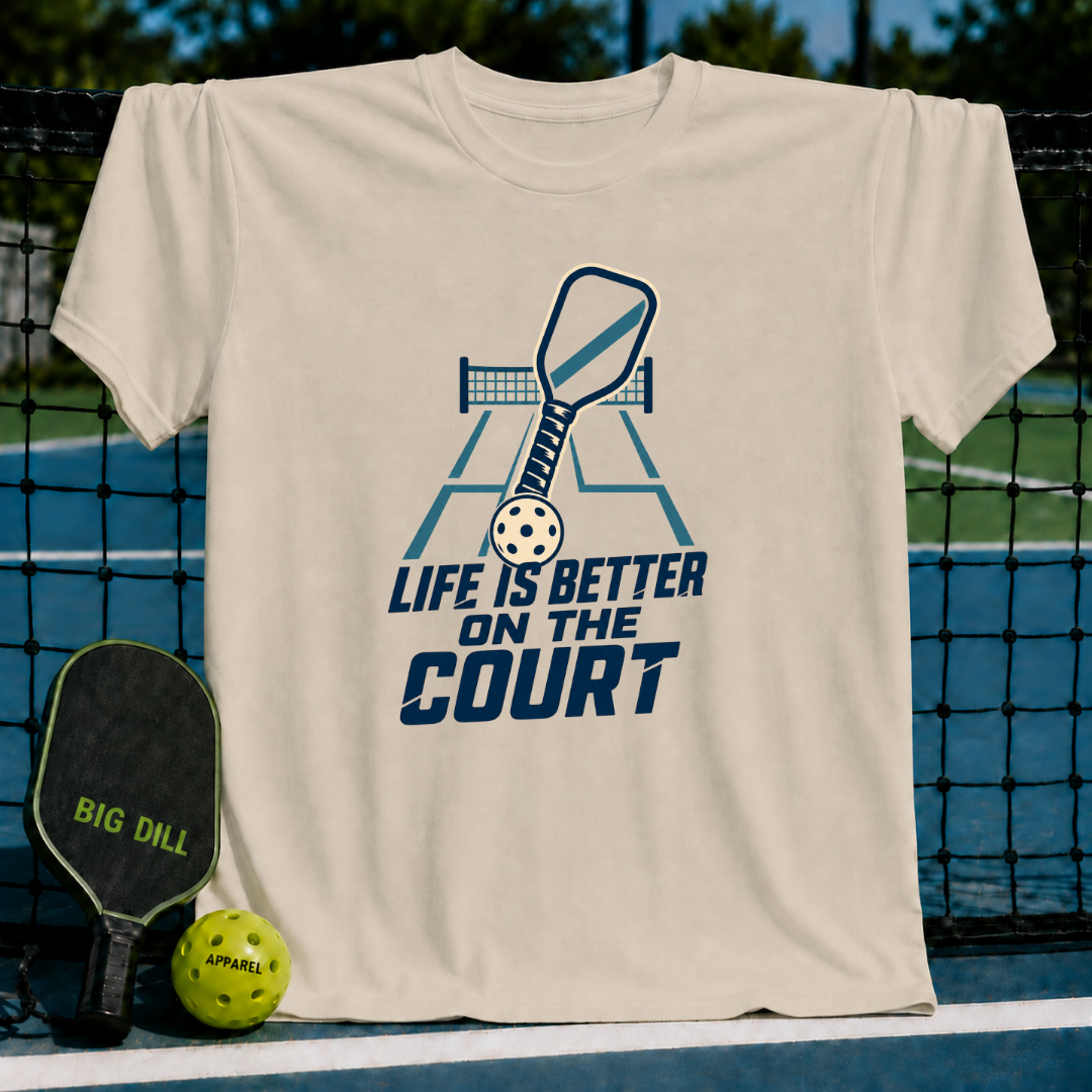 Beige crewneck t-shirt featuring a blue pickleball paddle, ball, and court graphic with the text Life is Better on the Court.