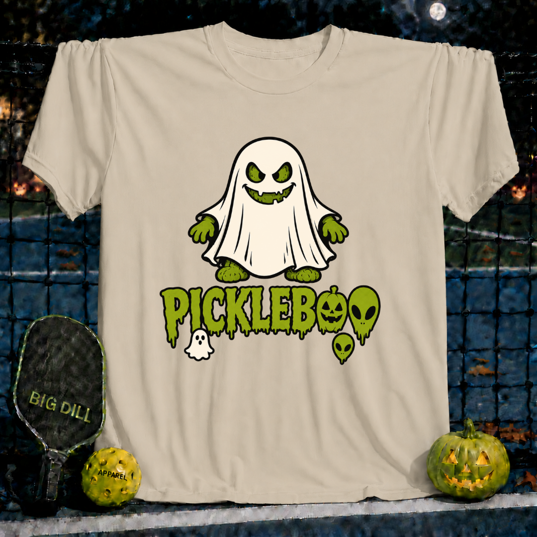 Sand-colored unisex PickleBoo t-shirt featuring a green ghost pickle graphic with spooky text on a pickleball court background.