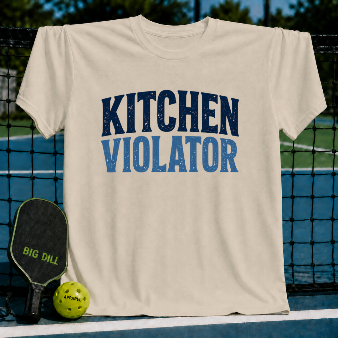 Cream-colored unisex t-shirt with distressed blue Kitchen Violator varsity lettering, displayed on a pickleball court.