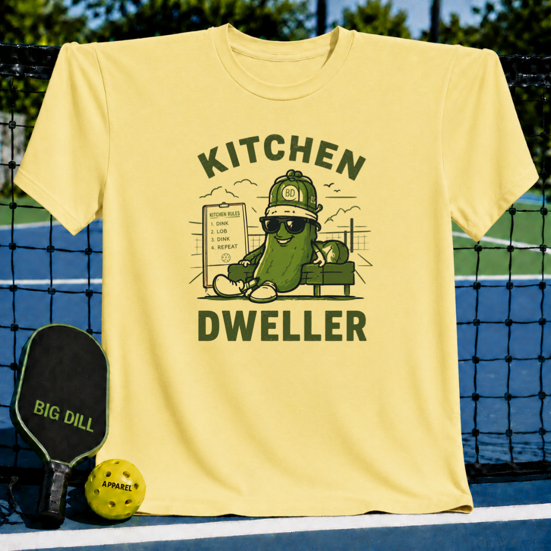 Light yellow crewneck t-shirt featuring a pickle character wearing sunglasses and a hat with Kitchen Dweller text.