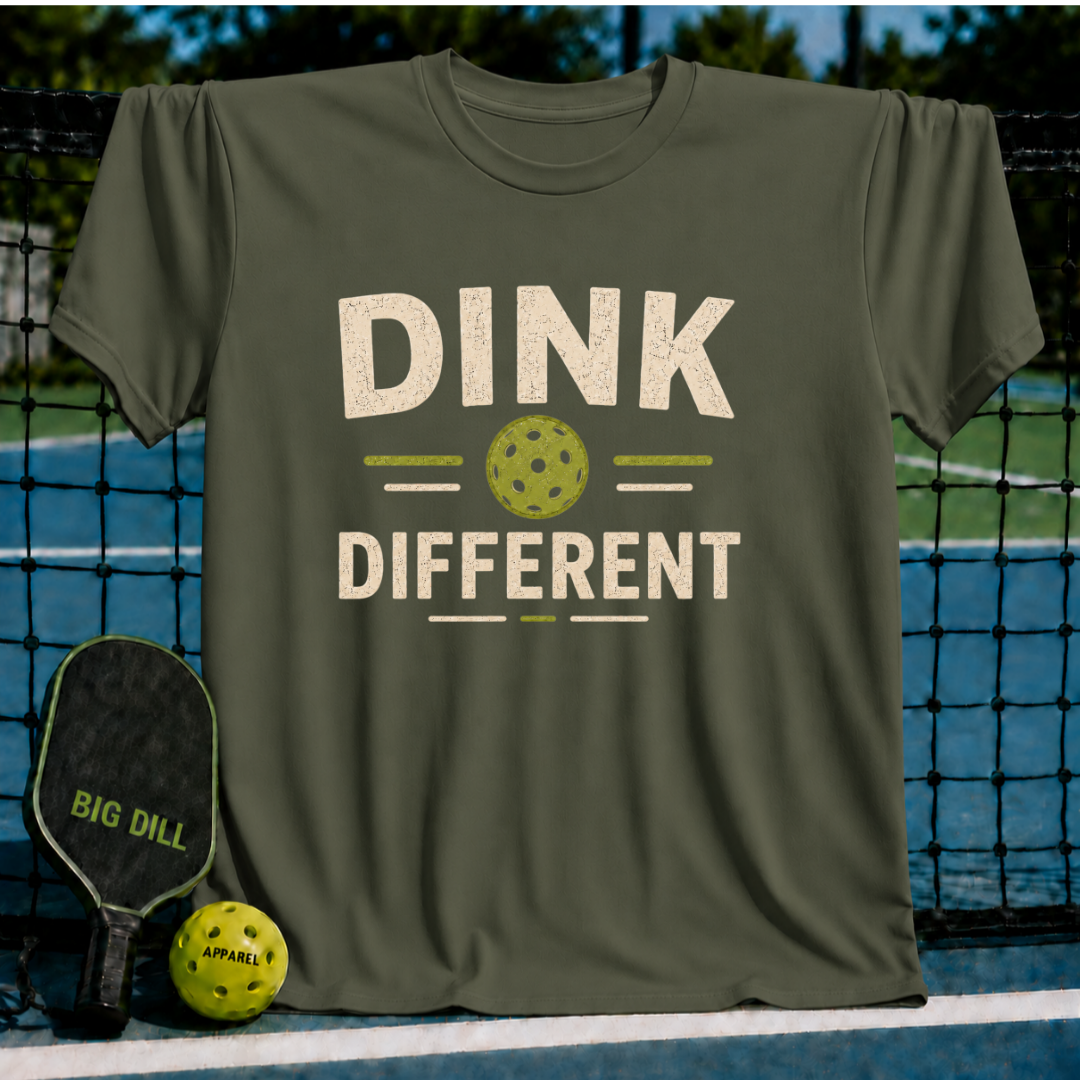 Olive green crew neck t-shirt featuring a distressed Dink Different pickleball graphic on a court background.