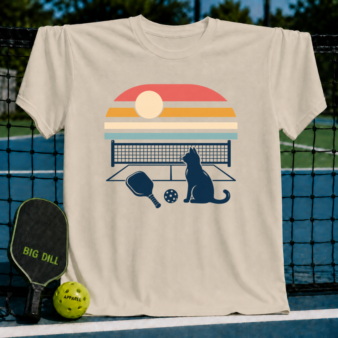 Beige crewneck t-shirt featuring a retro sunset graphic with a cat, pickleball paddle, and ball on a court background.