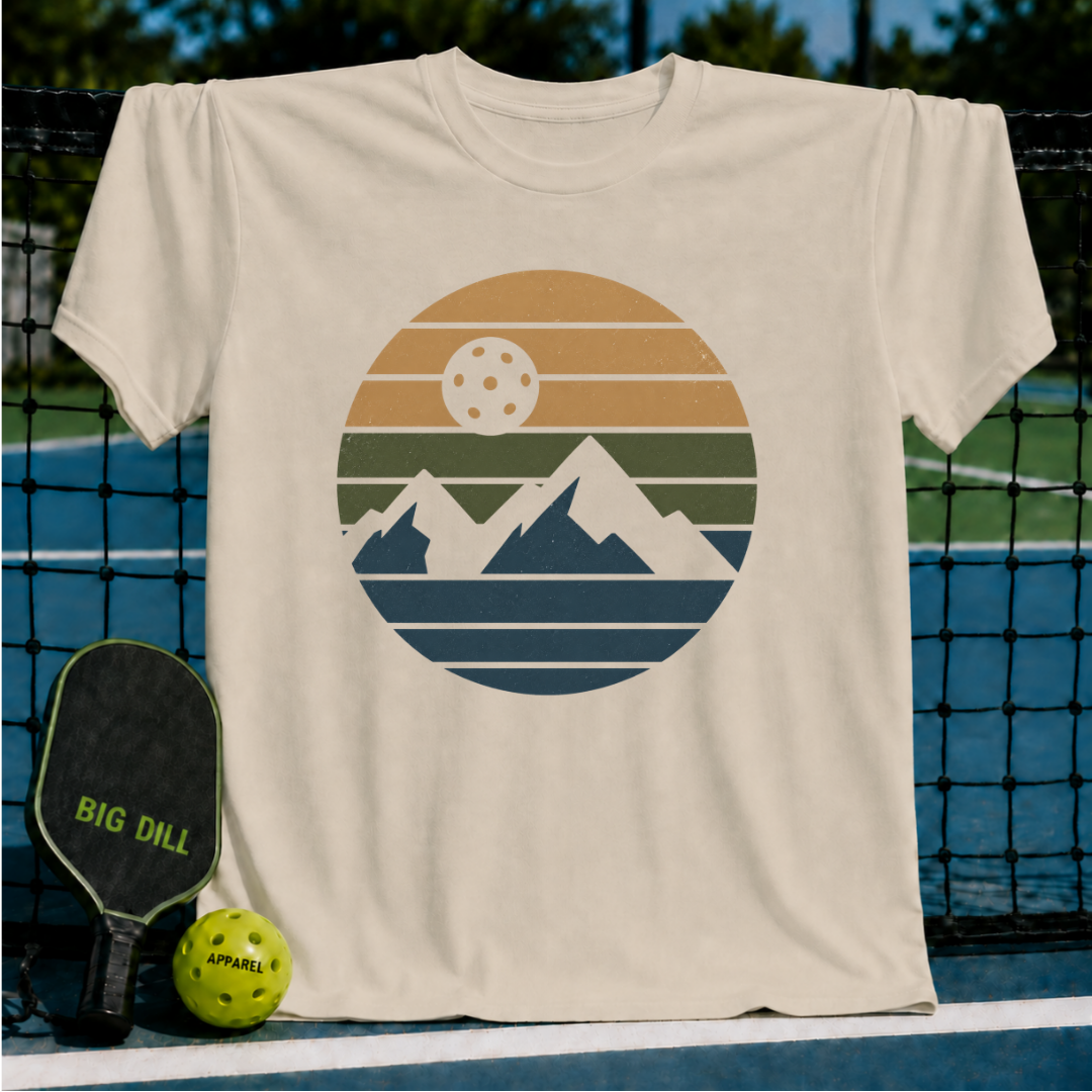 Cream unisex t-shirt featuring a retro circular graphic of mountains and a pickleball sun on a pickleball court.
