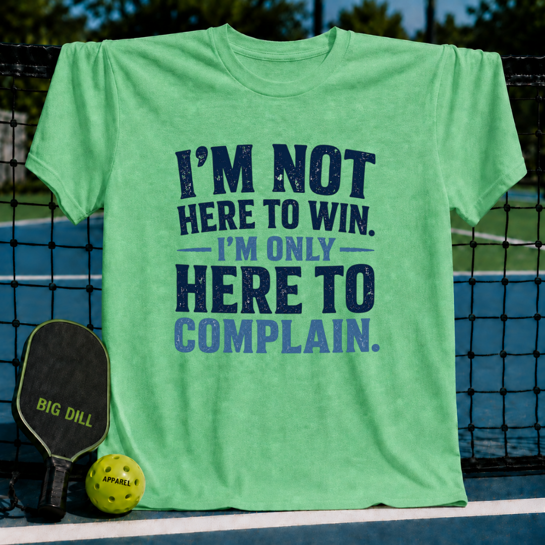 Light green unisex t-shirt with distressed navy blue text reading I'm Not Here To Win, I'm Only Here To Complain on a pickleball court.