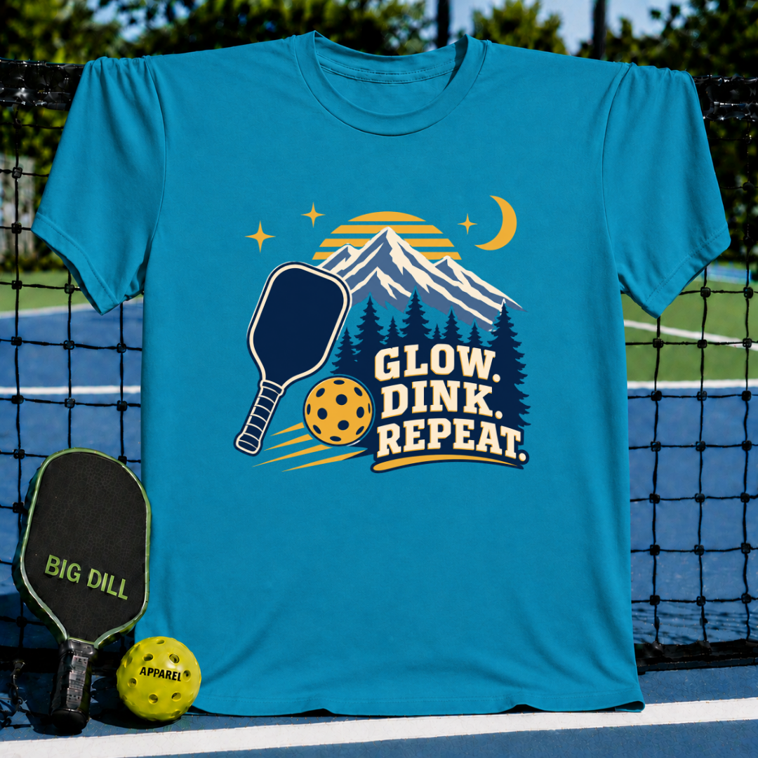 Bright blue crew neck t-shirt featuring a mountain, pickleball paddle, and ball graphic with Glow Dink Repeat text.