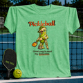 Light green unisex t-shirt featuring a cartoon pickle on crutches with a paddle and the text Pickleball: Great way to meet my deductible.