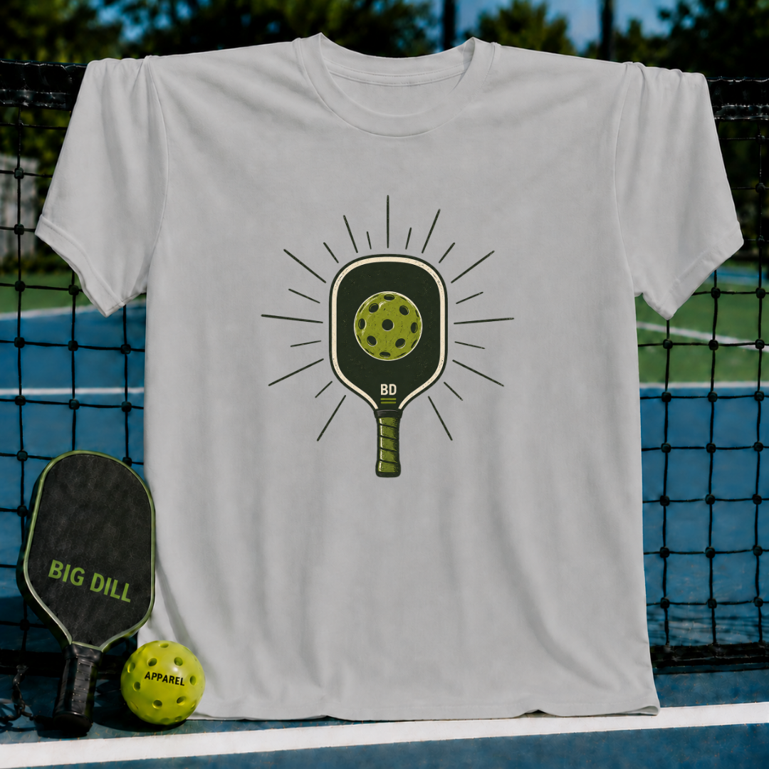 Light gray cotton t-shirt featuring a green pickleball paddle graphic with a sunburst design on a pickleball court background.