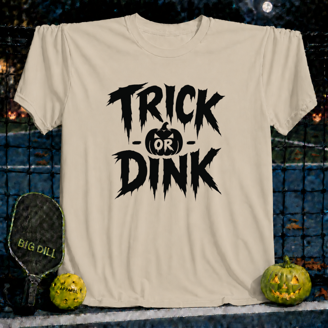 Sand-colored unisex t-shirt featuring a black Trick or Dink Halloween graphic with a pumpkin icon on a pickleball court background.