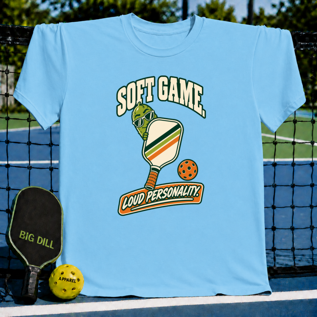 Light blue crew neck t-shirt featuring a pickle character with sunglasses, a pickleball paddle, and Soft Game text.