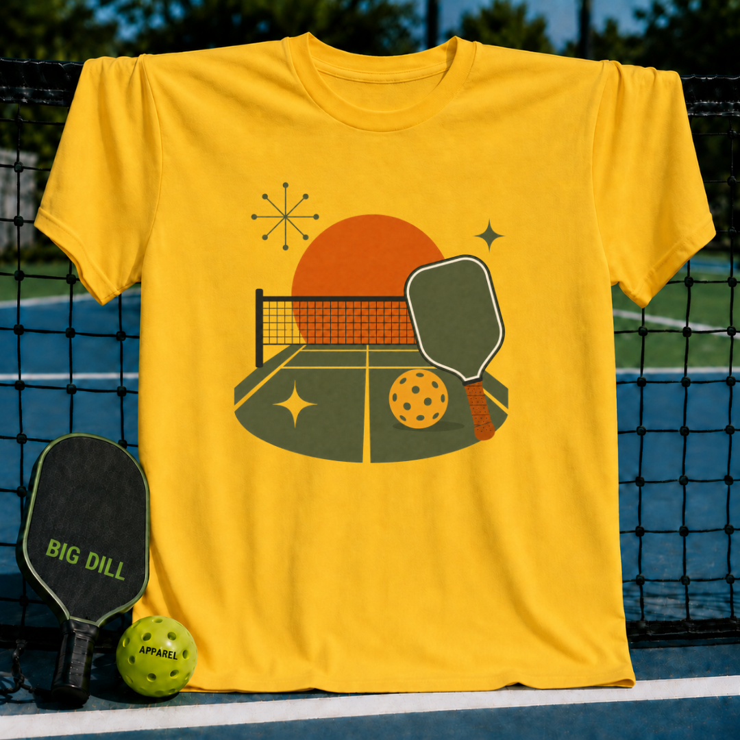 Bright yellow crewneck t-shirt featuring a retro midcentury pickleball court graphic with a paddle and ball.