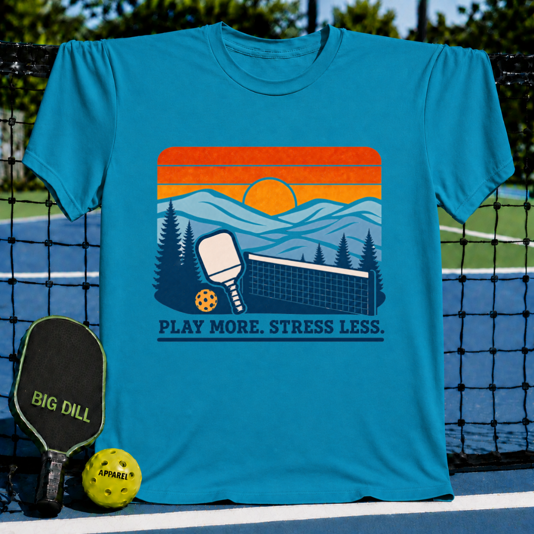 Blue cotton t-shirt featuring a retro pickleball sunset graphic with the text Play More. Stress Less.