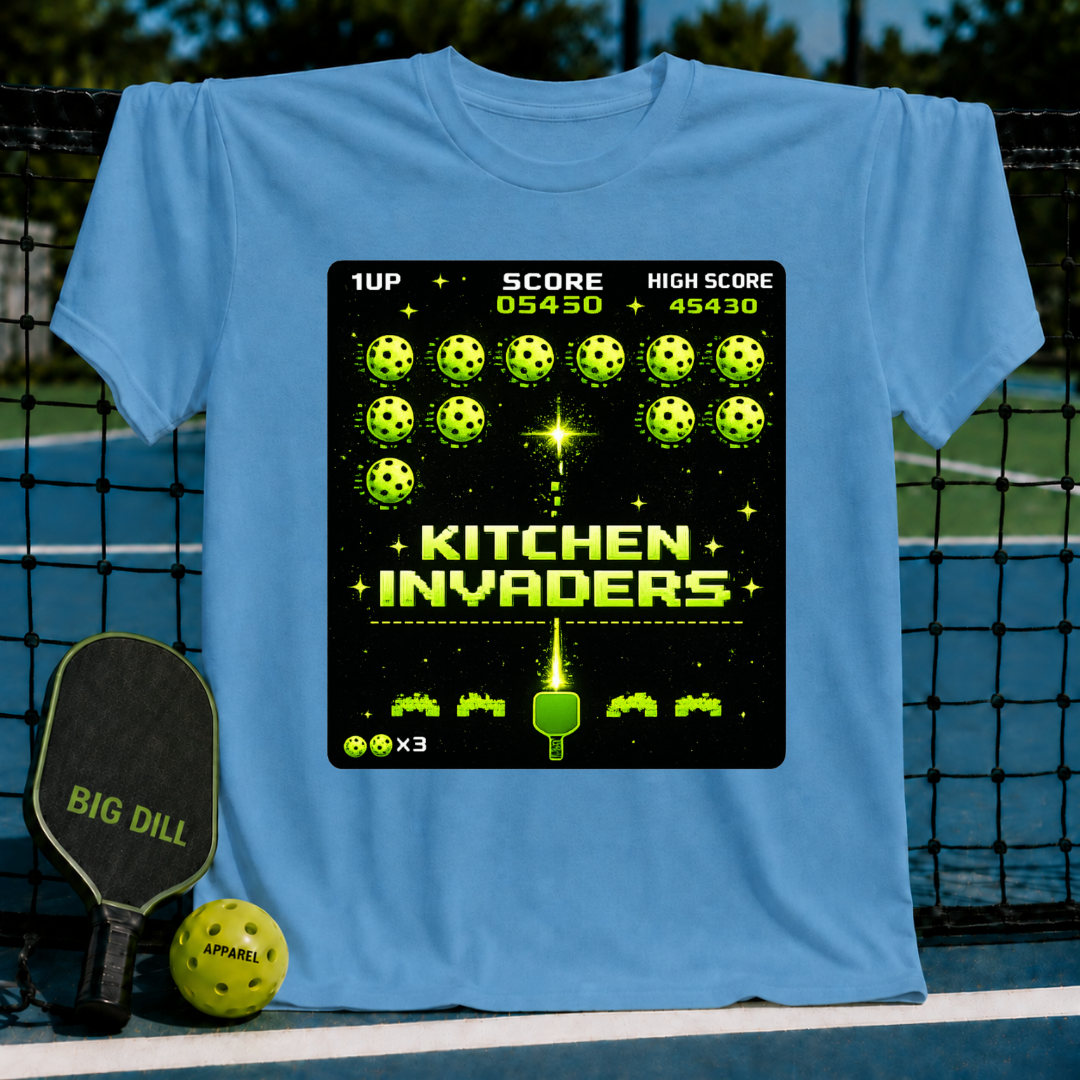 Light blue unisex t-shirt featuring a pixel-art Kitchen Invaders graphic with neon green pickleballs and a paddle.