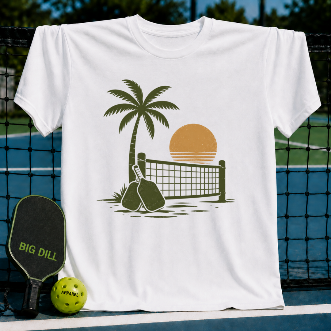 White unisex t-shirt featuring a retro palm tree, pickleball net, and paddle graphic in olive green and sunset orange.