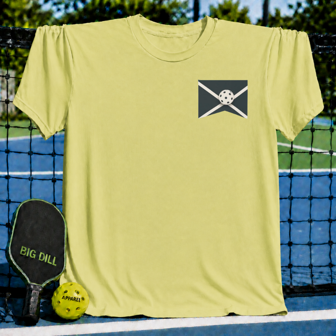 Light yellow unisex t-shirt featuring a small pickleball graphic on the chest, displayed against a pickleball court backdrop.