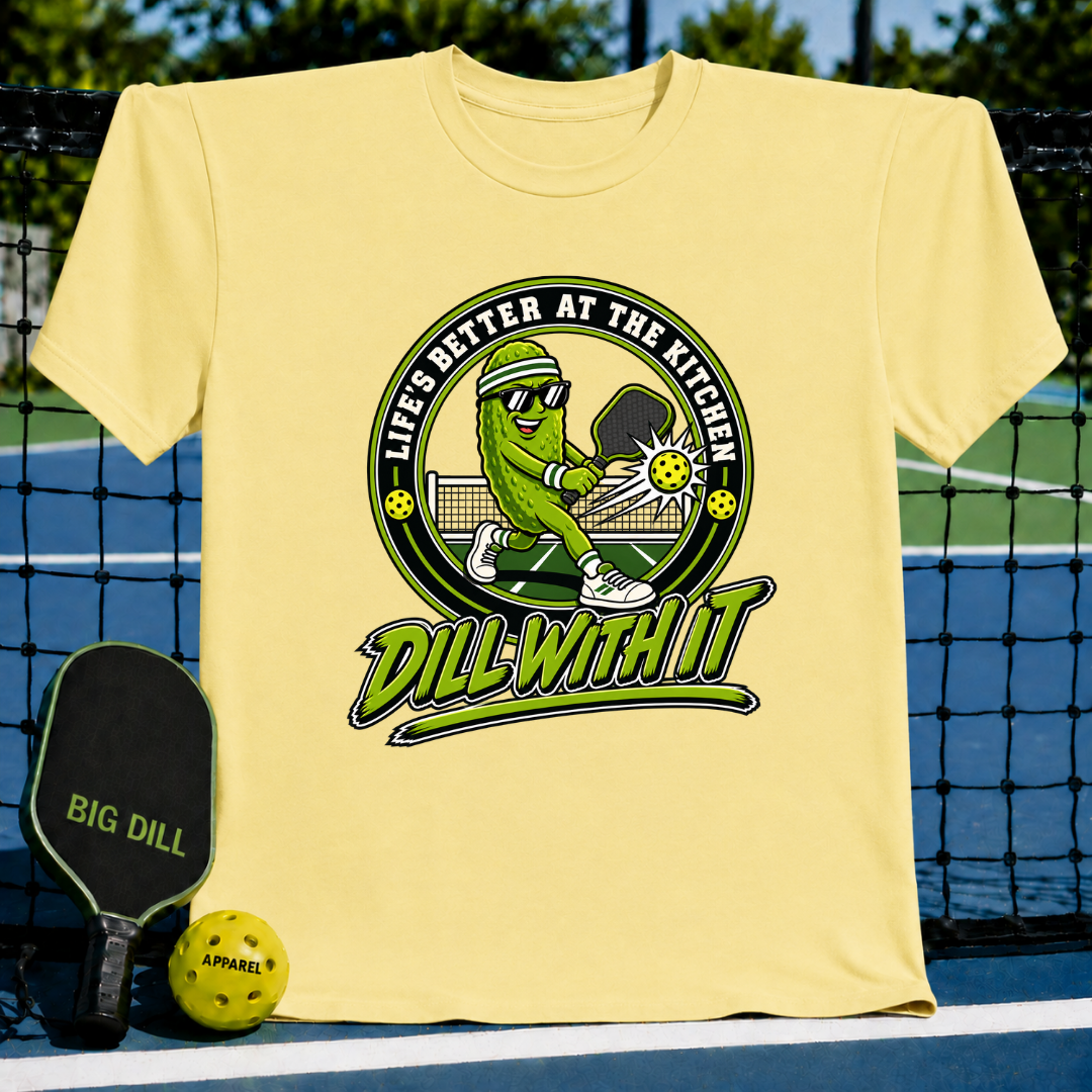Light yellow crewneck t-shirt featuring a pickleball-playing pickle graphic with the text Dill With It and Life's Better at the Kitchen.