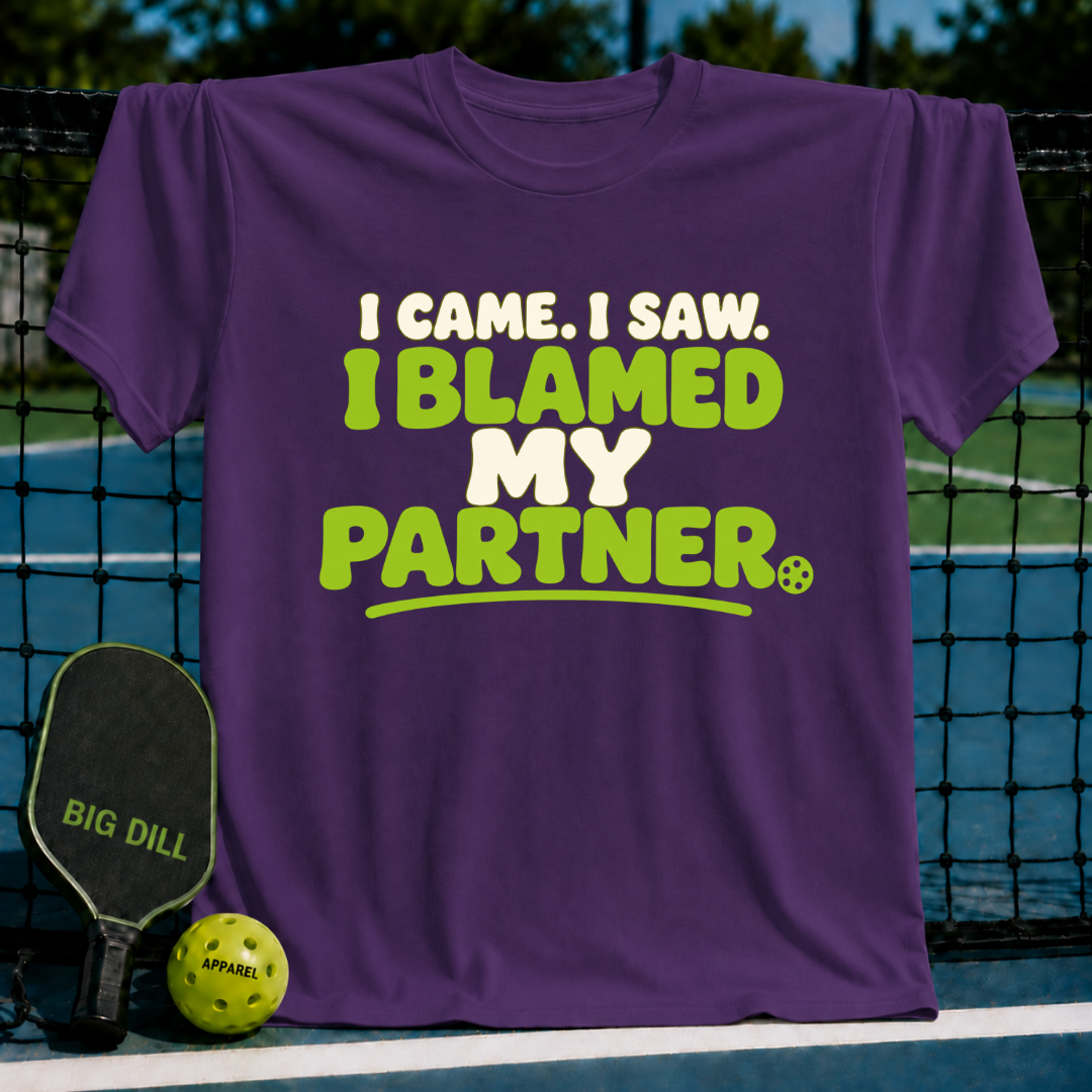 Purple crewneck t-shirt with lime green and white text reading I Came, I Saw, I Blamed My Partner, on a pickleball court.