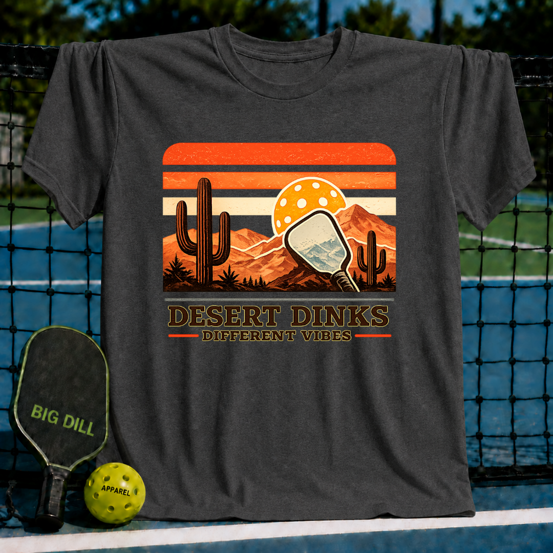Charcoal grey Desert Dinks t-shirt featuring a retro sunset, cactus, and pickleball paddle graphic on a pickleball court.