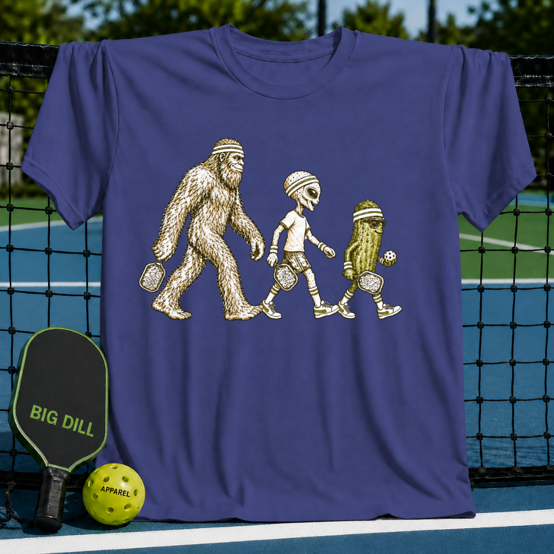 Purple crewneck t-shirt featuring a graphic of Bigfoot, an alien, and a pickle playing pickleball on a court.
