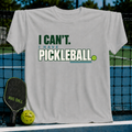 Light gray crew neck t-shirt featuring the text I Can't I Have Pickleball in green and blue with a small ball graphic.