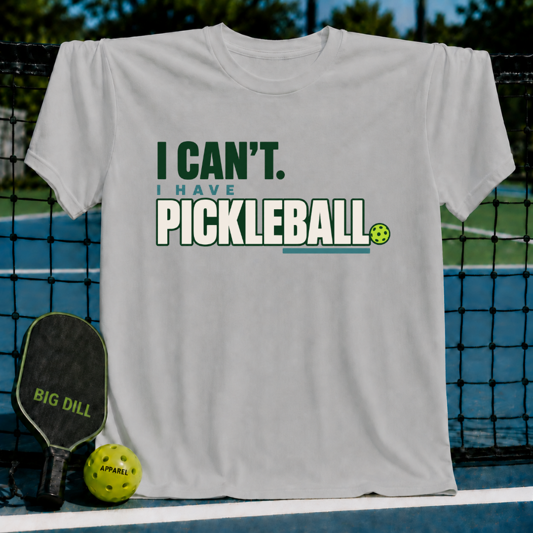 Light gray crew neck t-shirt featuring the text I Can't I Have Pickleball in green and blue with a small ball graphic.