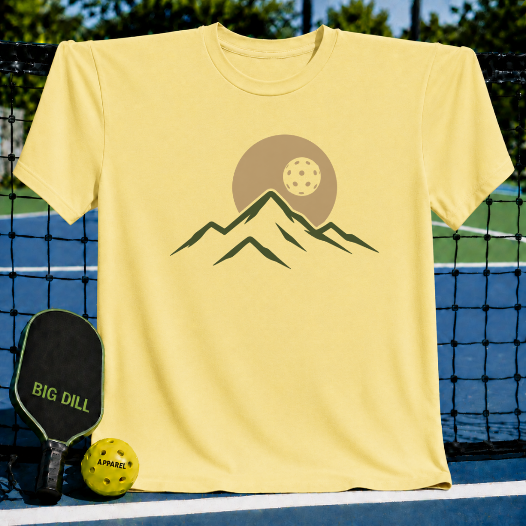 Soft yellow unisex t-shirt featuring a minimalist mountain and pickleball eclipse graphic, displayed on a pickleball court.